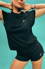 Person wearing a black sleeveless top and shorts with a logo on a teal background